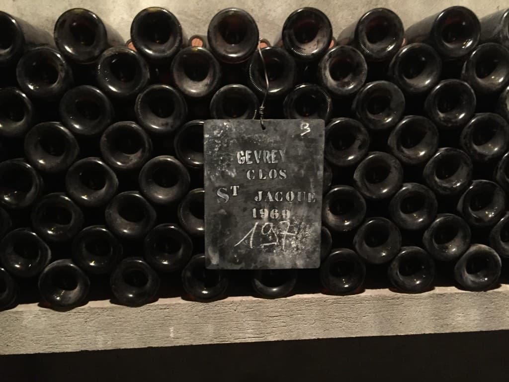 Vintage bottles in a cellar with a handwritten Gevrey Clos Saint-Jacques 1969 tag